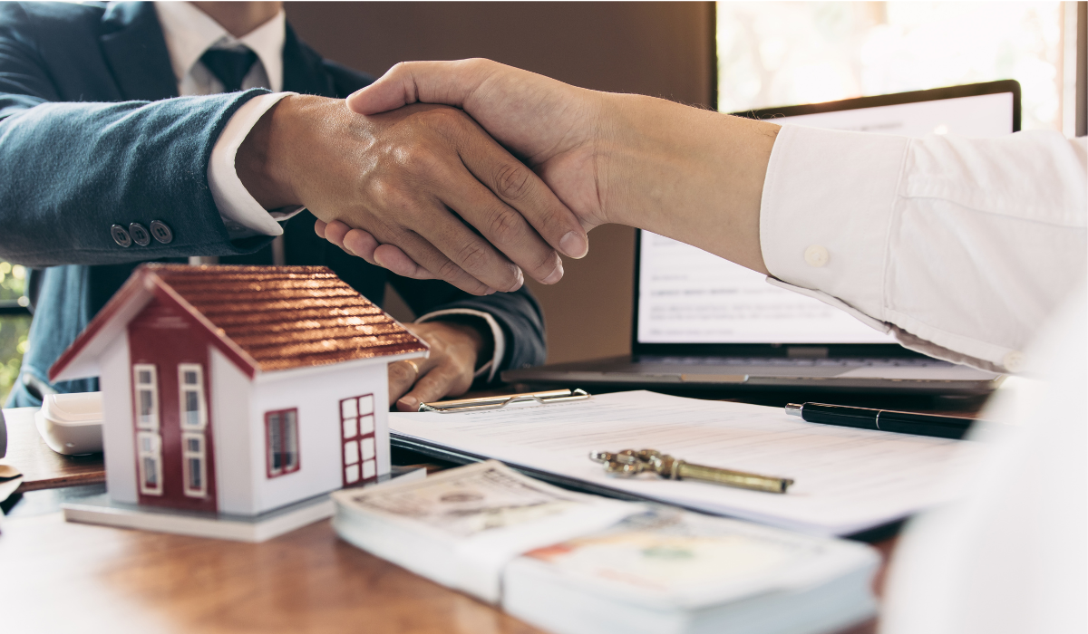two people shaking hands over a house model